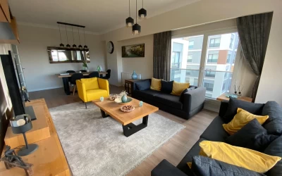 living-room-with-two-gray-sofas-and-yellow-armchair-wooden-coffee-table-broad-windows-dining-table-and-pendant-lights